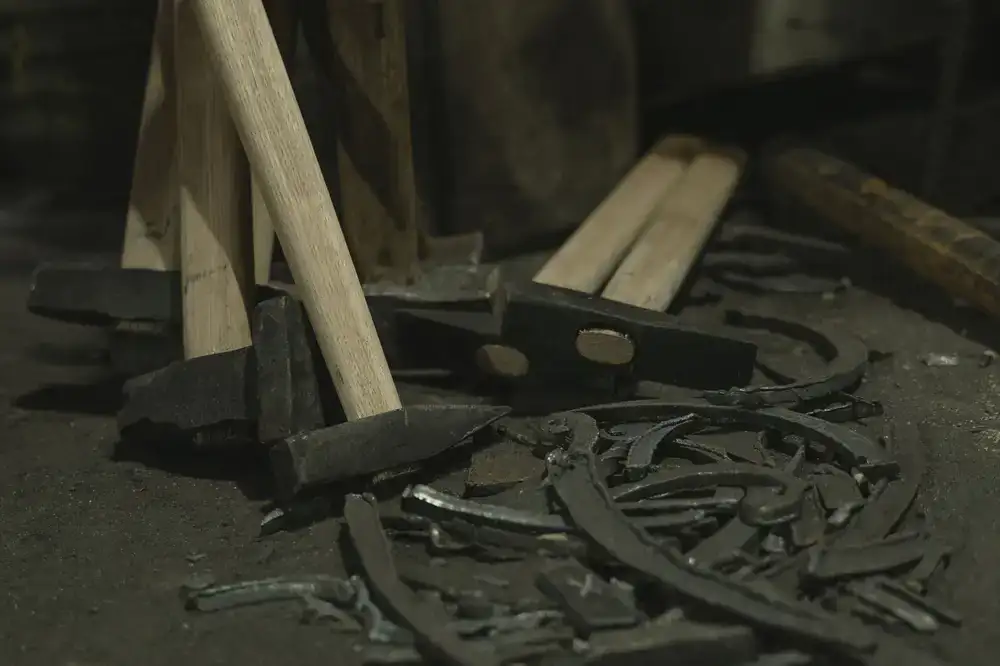 Traditional mosaic hammer resting beside cut marble pieces on a wooden workbench